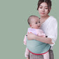 Mother carrying baby in a soft green cotton baby sling wrap for comfortable hands-free support