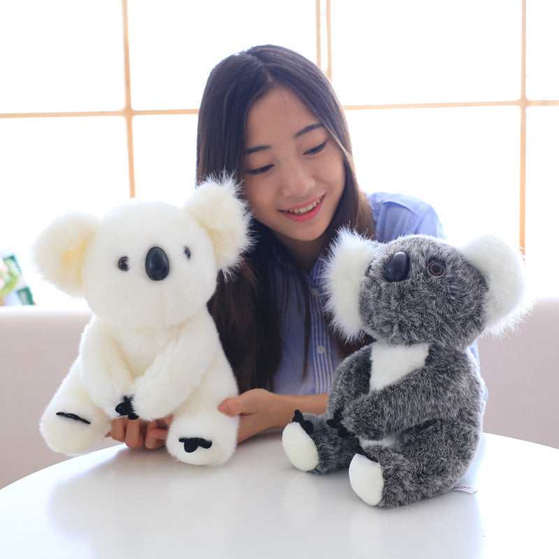 Woman holding white and grey koala plush toy for kids sitting at table indoors